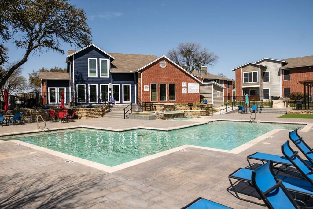 A swimming pool surrounded by blue lounge chairs and a building in the background.