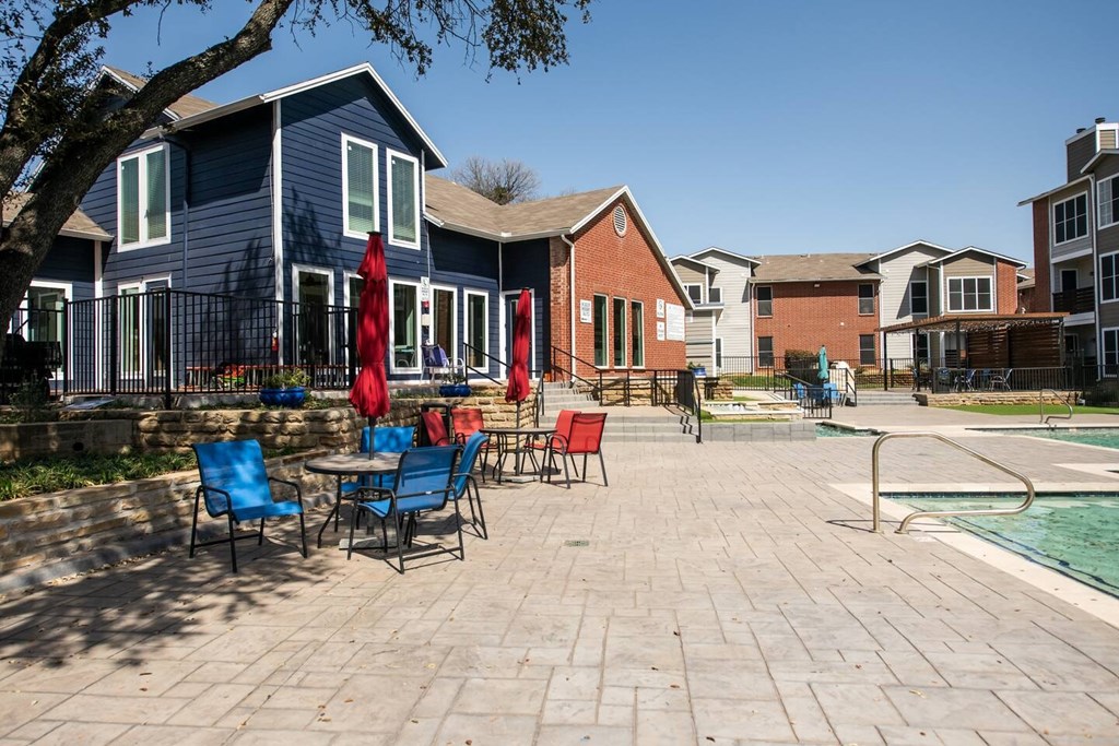 A patio with chairs and umbrellas is surrounded by houses.