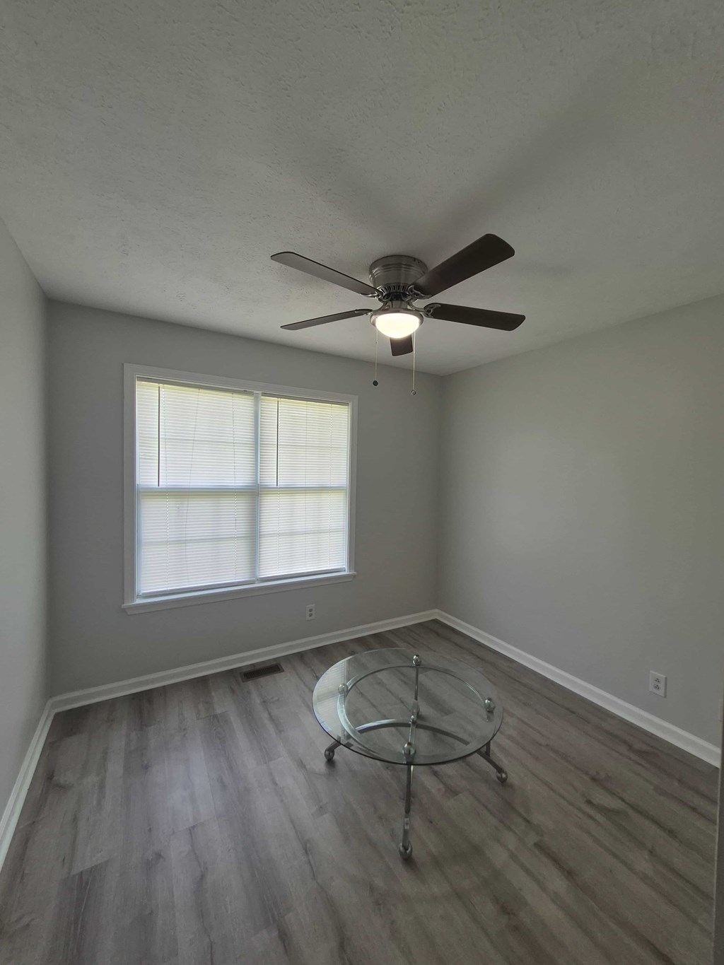 A room with a ceiling fan and a glass table.