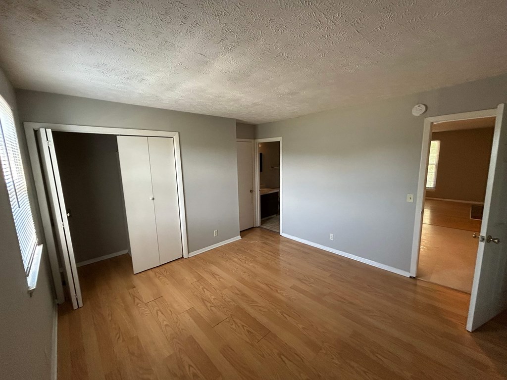 A room with wooden floors and white walls, with a door on the left and another on the right.