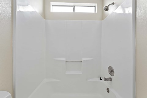 A white bathroom with a window above the tub.