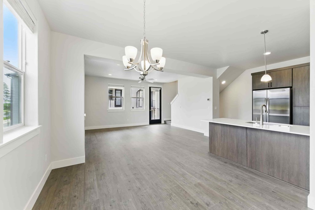 A spacious living room with a chandelier and a kitchen area in the background.