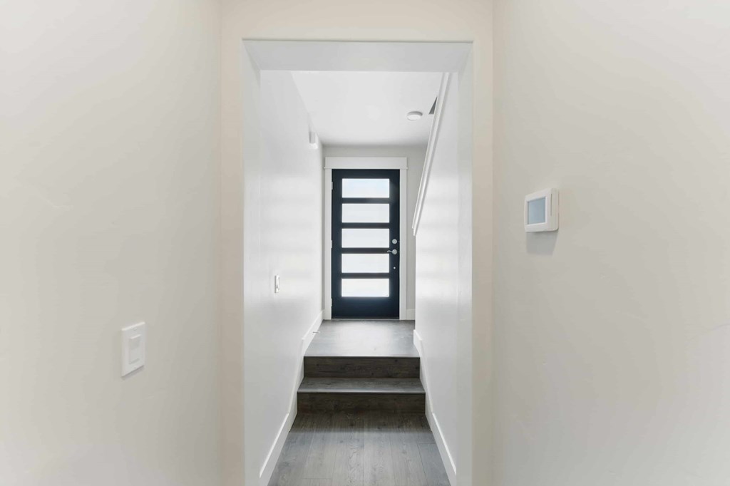A hallway with a black door and a light switch on the wall.