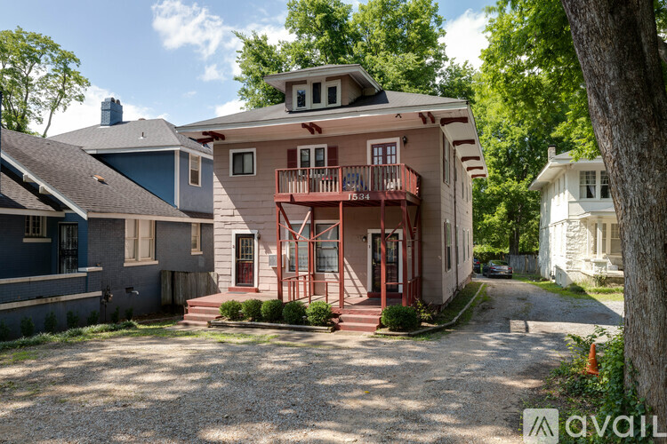 A house with a red door and a balcony is surrounded by trees.