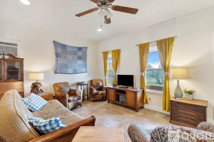 A living room with a sofa, armchairs, a television, and a fan.