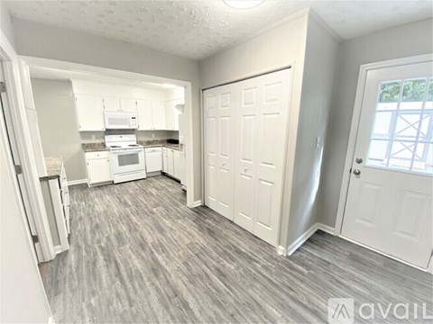 A kitchen area with white cabinets and a fridge, a door, and a window.