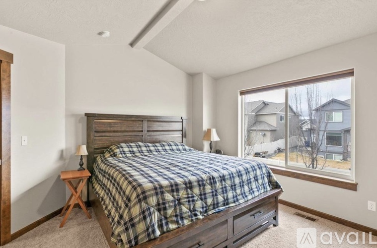 A bedroom with a bed, a small table, and a window overlooking a residential area.