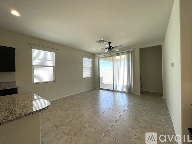 A spacious room with a fan, tiled floor, and sliding glass doors leading to a balcony.