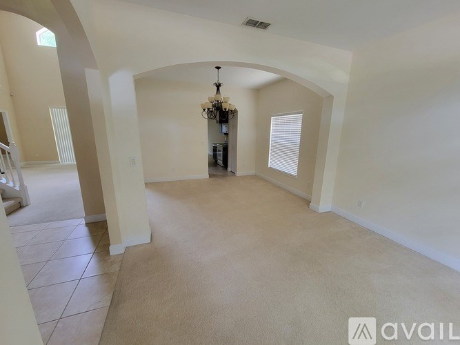 A spacious living room with a chandelier and a staircase on the left.