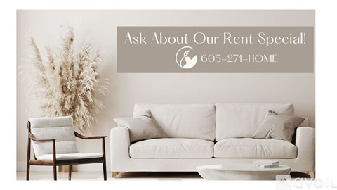 A living room with a white couch and a chair, a potted plant, and a sign offering a rent special.