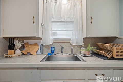 A kitchen with a sink under a window with curtains.