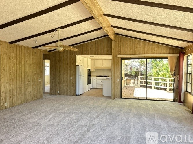 A spacious room with wooden walls and ceiling, a fan, and a carpeted floor.