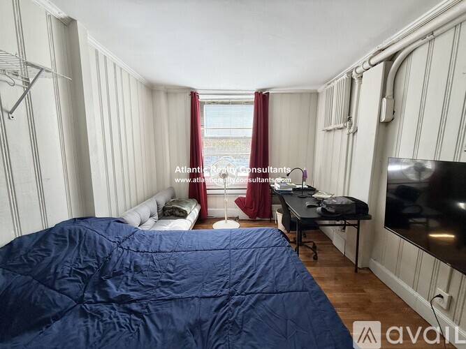 A bedroom with a bed, a window with curtains, and a flat-screen TV mounted on the wall.