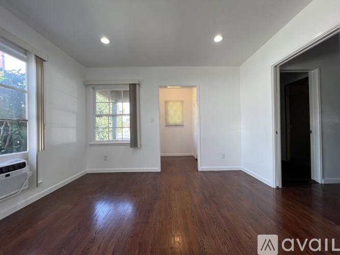 A room with wooden floors and white walls, with a window and a door visible.