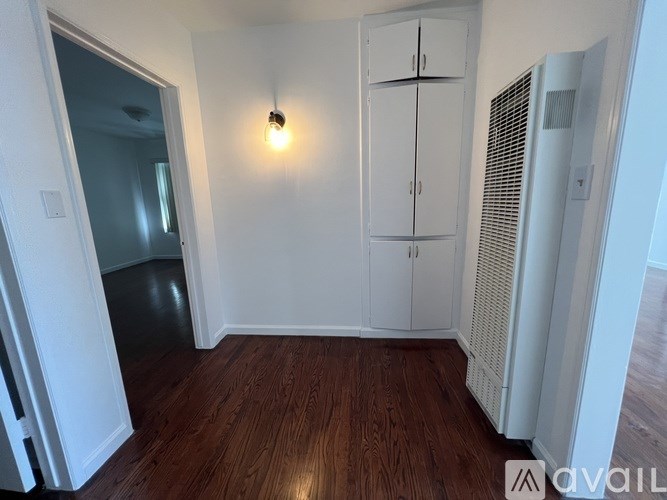 A room with a wooden floor, a white wall, a white cabinet, and a white air conditioner unit.