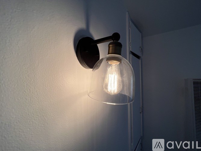 A wall-mounted light fixture with a clear glass shade is turned on.