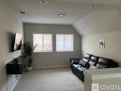 A living room with a black leather couch and a flat screen TV mounted on the wall.