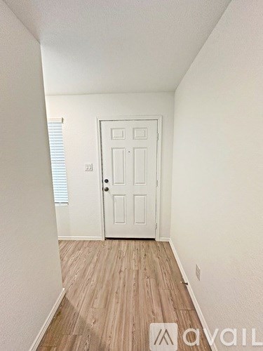 A white door is in the middle of a hallway with wood flooring.