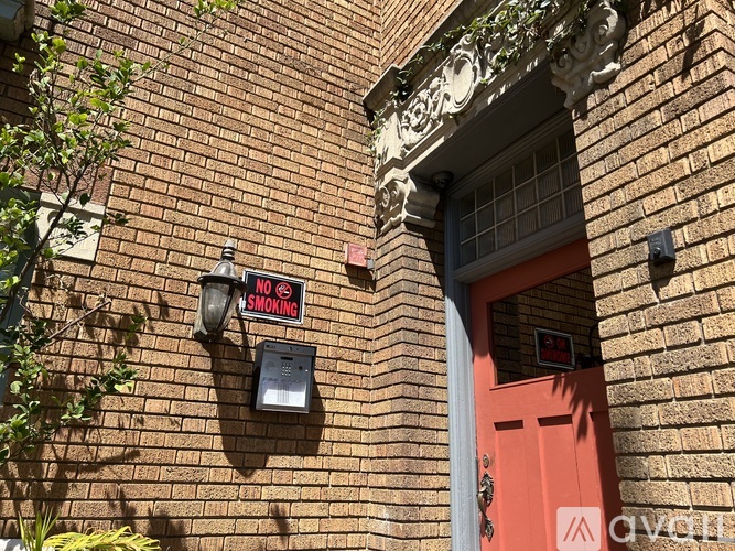 A red door is on the right side of a brick wall with a sign that says "NO SMOKING" on the left side.