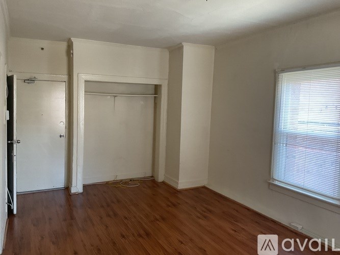 A room with wooden floors and white walls, with a window on the right side.
