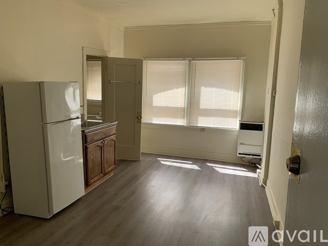 A kitchen with a refrigerator, wooden cabinets, and a window with blinds.