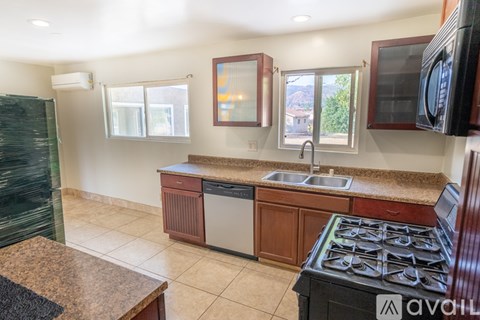 A kitchen with a black stove top oven and a sink with a window above it.