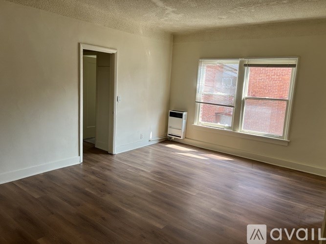 A room with wooden floors and a window with a view of a brick building outside.