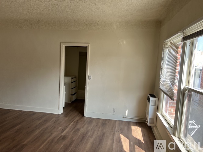 A room with a doorway leading to another room, a window with blinds, and a floor heater.