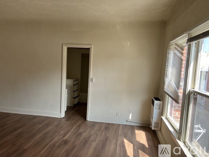 A room with a doorway leading to another room, a window with blinds, and a floor heater.