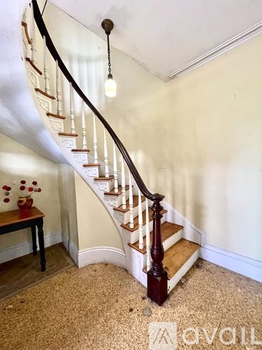 A wooden staircase with a curved banister and a light hanging from the ceiling.