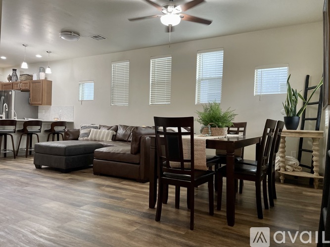 A living room with a brown leather couch, a wooden dining table with chairs, and a kitchen area with a refrigerator and cabinets.