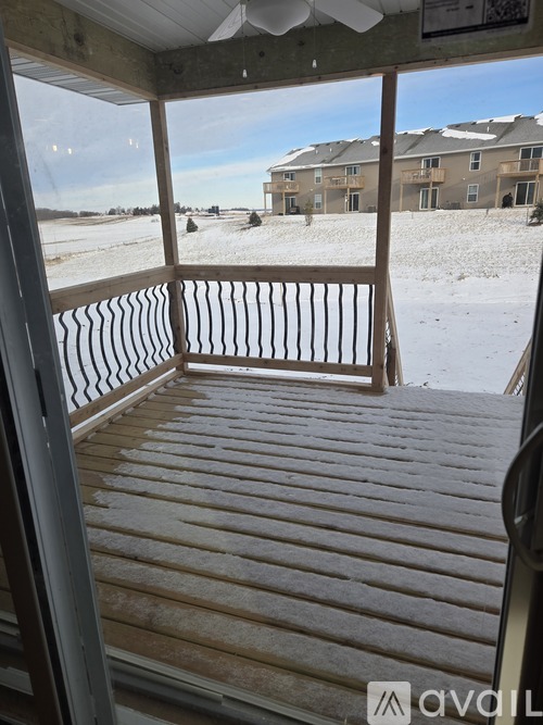 A wooden deck with a railing and a view of a snowy landscape and buildings in the distance.