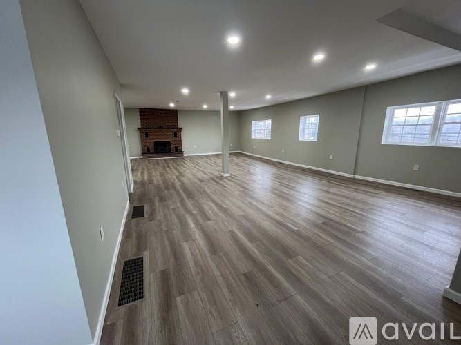 A spacious room with wooden flooring and a fireplace in the corner.