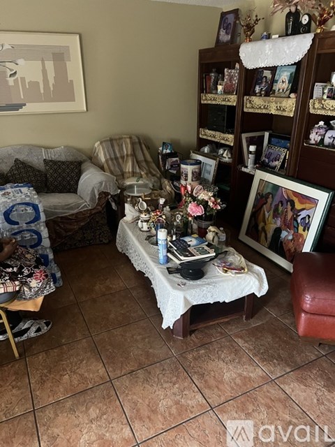 A woman is sitting on a chair in a living room with a couch, a coffee table, and a bookshelf.