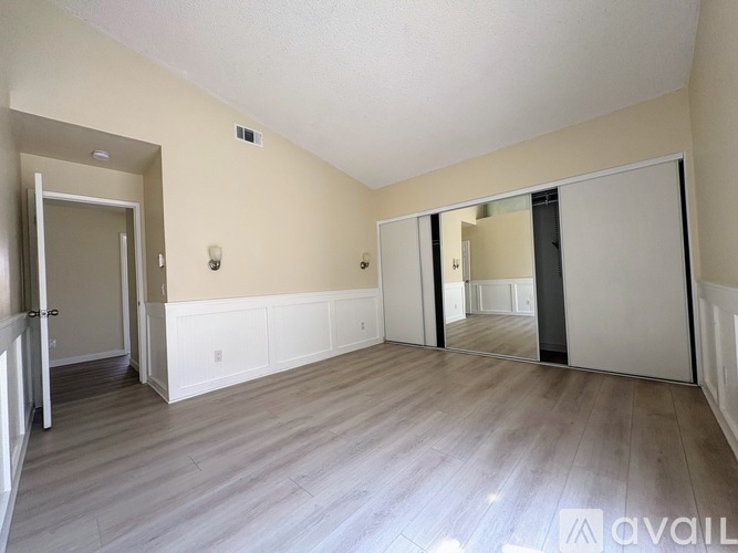 A spacious room with wooden flooring and white walls.