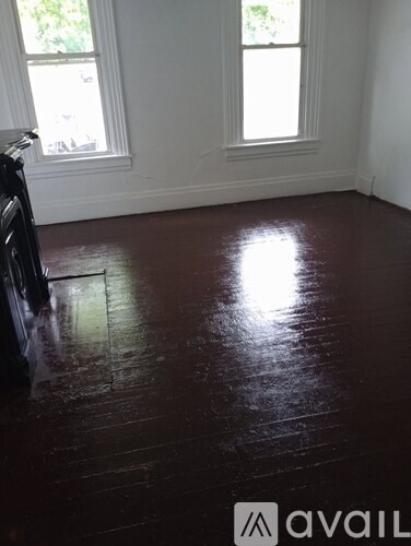 A room with dark wood flooring and two windows.