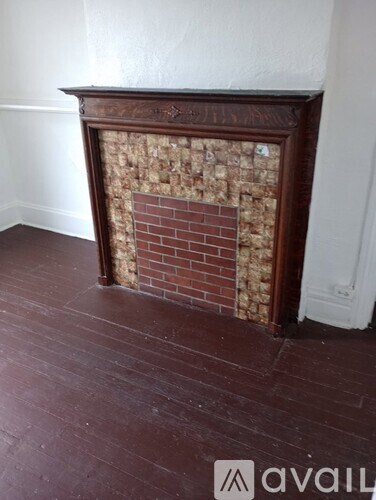 A fireplace with a wooden frame and a brick insert sits in a room with wooden flooring.