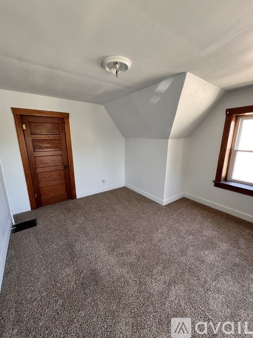 A room with a carpeted floor, a wooden door, and a window with a white ceiling.