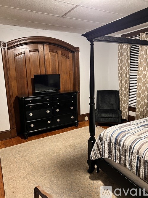 A bedroom with a four poster bed and a wooden dresser.