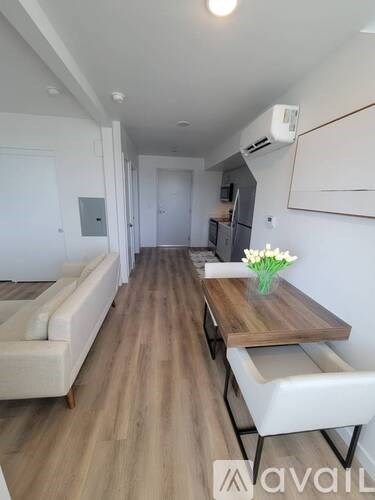 A long, narrow room with a white couch, a wooden table with a vase of flowers, and a kitchen area in the background.