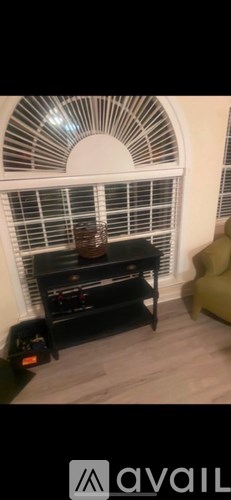 A black shelf with a bottle on it in front of a window with white blinds.