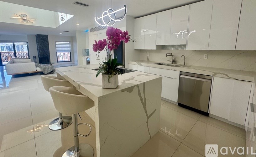 A kitchen with white cabinets and a marble island with a vase of flowers on it.