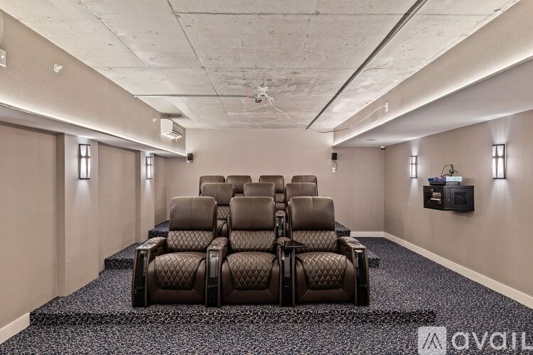A row of black leather seats in a room with a wall-mounted television.