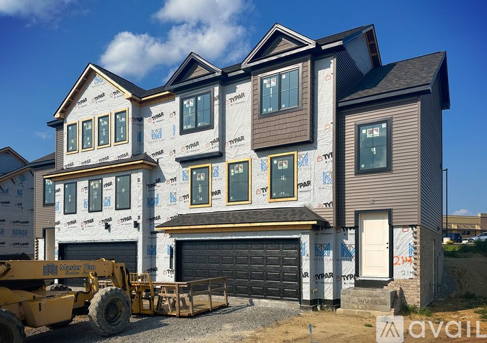 A house under construction with a yellow excavator in front.