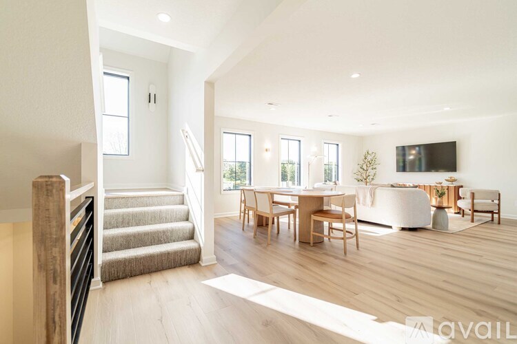 A spacious living room with a staircase on the left and a dining area in the center.