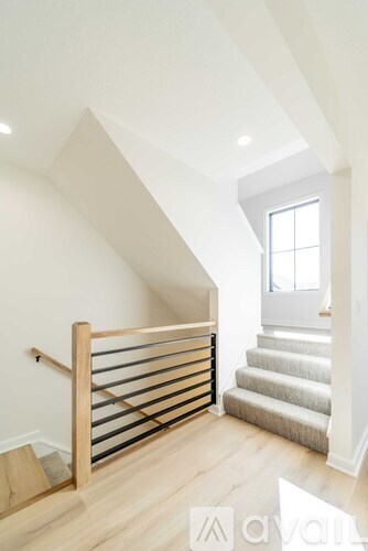 A wooden staircase with a metal railing leads to a bright room.