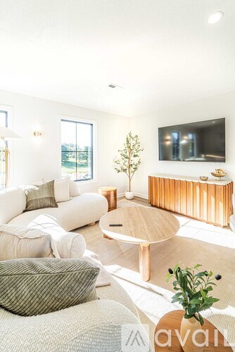 A living room with a white couch, a wooden coffee table, and a television mounted on the wall.