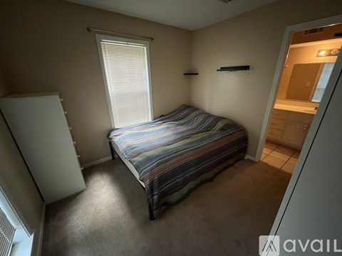 A bedroom with a bed, a window with blinds, and a white refrigerator.