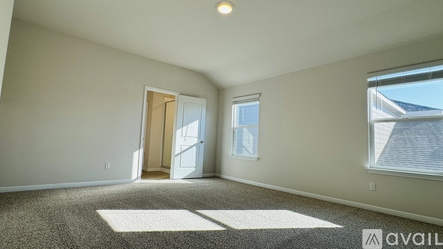 A room with a carpeted floor and a window with a view of the roof of a building.