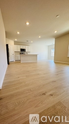 A spacious room with wooden flooring and a kitchen area in the background.